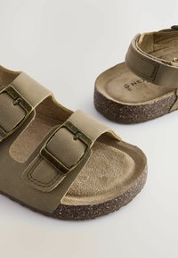 Oliven grønne sandaler med to justerbare remme, metalspænder og en tekstureret fodseng, der har en lysebrun korksål.