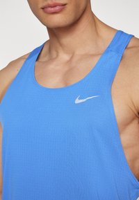 Camiseta sin mangas deportiva de color azul con textura transpirable y pequeño logo blanco de Nike en la parte superior izquierda del pecho.