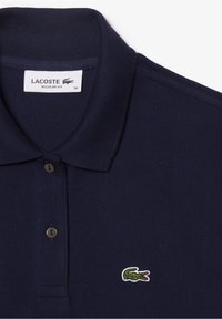 Polo Lacoste bleu marine avec deux boutons, un col côtelé et un logo crocodile vert sur la poitrine. Coupe régulière, taille 36.