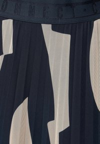 Gonna plissettata con un motivo geometrico in navy e crema. Presenta un tessuto a rete testurizzato e una vita robusta con la scritta "CONNECT" in rilievo.