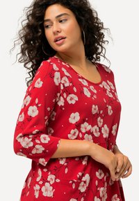 Rotes Blumenkleid mit drei Viertelärmeln, verziert mit weißen und rosa Blumenmustern, aus weichem Stoff und mit Rundhalsausschnitt.