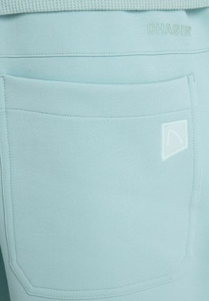Light blue fabric close-up showing a large stitched pocket with a small triangular logo and embossed "CHASIN" text near the waistband.