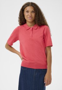 Polo à manches courtes couleur corail vif, en coton doux, avec col, patte à trois boutons et détail de bord-côte à l'ourlet.