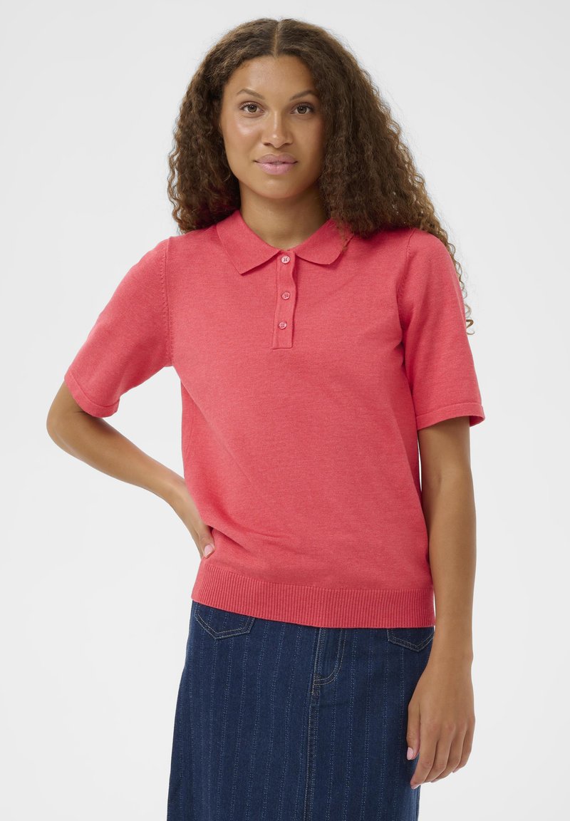 Polo à manches courtes couleur corail vif, en coton doux, avec col, patte à trois boutons et détail de bord-côte à l'ourlet.