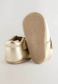 Auksinės odinės kūdikių bateliai su suede padais, apvalaus pirštų dizaino, šonine juostele ir lygia apdaila. Minkšta tekstūra ir minimalūs siuvimo detalės.