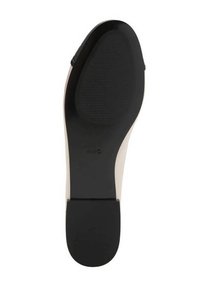 Suela de un zapato beige con un tacón negro y un agarre de goma negro texturizado en la parte delantera y en el área del talón.