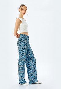 Breda byxor i ett blått och svart geometriskt mönster, gjorda av lättviktsmaterial. Kombinationen med en vit åtsittande crop top.