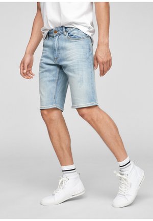 Shorts en denim bleu clair avec une coupe classique, présentant un délavé, un design à 5 poches et un ourlet brut. Portés avec des baskets blanches et des chaussettes rayées.