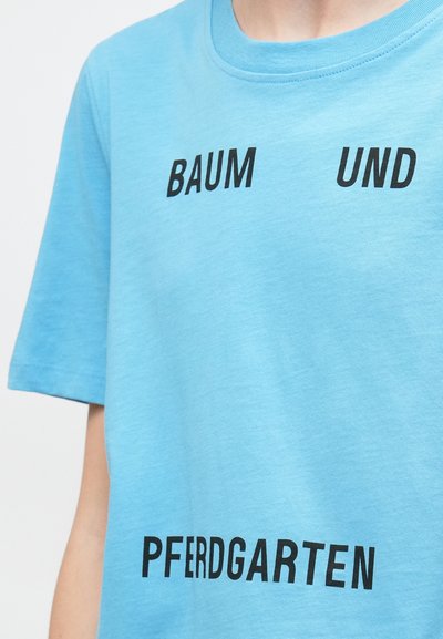 Ανοιχτό μπλε βαμβακερό μπλουζάκι με έντονα μαύρα γράμματα που λένε "BAUM UND PFERDGARTEN" σε κεντρική διάταξη. Μαλακή υφή, στρογγυλή λαιμόκοψη.