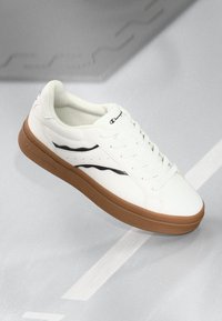White sneaker with a smooth leather upper, black accent stripes, round toe, and a light brown rubber sole. Lace-up design.