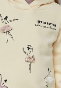 Kremowa bluza z kapturem z czarnymi szkicami baletnic, różowymi i białymi zdobieniami tutu oraz napisem "ŻYCIE JEST LEPSZE, kiedy tańczysz" na klatce piersiowej.