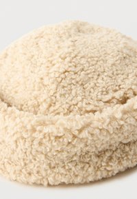Runde, cremefarbene Beret aus softem, strukturiertem Stoff mit einer flauschigen Oberfläche, die ein einfaches, unembellisches Design aufweist.