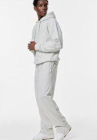 Lichtgrijze, katoenen hoodie met een voorzak en bijpassende sweatpants. Heeft een capuchon met trekkoord en een relaxte pasvorm. Witte sneakers.