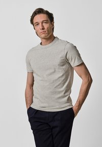 Jasnoszary t-shirt z krótkim rękawem, wykonany z miękkiego materiału. Posiada okrągły dekolt i dopasowany krój, w zestawie z granatowymi spodniami.