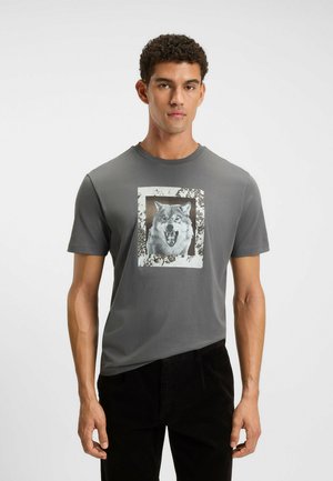 T-shirt grigio a maniche corte con una grafica di un lupo che ringhia all'interno di un rettangolo bianco invecchiato. Tessuto in cotone morbido.