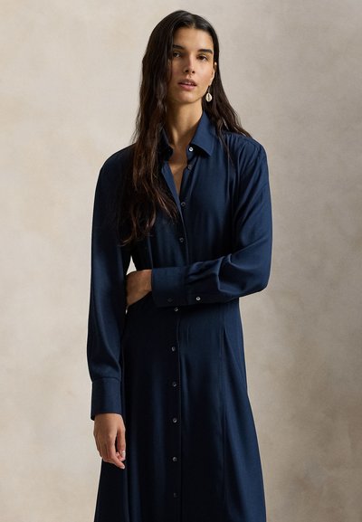 Φόρεμα μακρυμάνικο σε σκούρο μπλε χρώμα, κατασκευασμένο από λεία ύφανση με κούμπωμα μπροστά, γιακά και άνετη εφαρμογή, σχεδιασμένο με διακριτικές πιέτες.