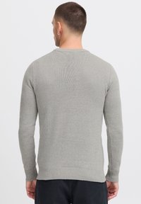 Gray knit sweater with long sleeves, round neckline, and ribbed hem. Fabric features a subtle texture and is slightly fitted at the waist.