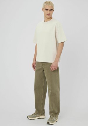 T-shirt crème oversized, pantalon olive, et baskets grises. Design simple avec des coupes droites et une coupe décontractée. Texture de tissu douce.
