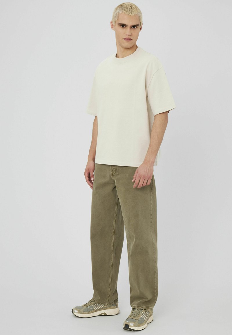 T-shirt crème oversized, pantalon olive, et baskets grises. Design simple avec des coupes droites et une coupe décontractée. Texture de tissu douce.