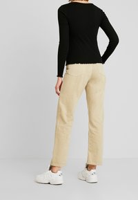 Zwarte ribbel longsleeve met golfrand, gecombineerd met tan rechte broek met achterzakken, gedragen met witte sneakers.