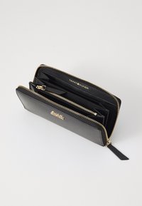 Melnas ādas maku ar zelta detaļām, ar rāvējslēdzēju, vairākiem nodalījumiem un redzamu zīmolu. Gluda tekstūra un taisnstūra forma.