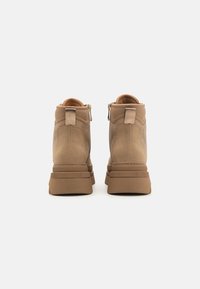 Bottes ankle marron avec une finition en cuir lisse, conçues avec une semelle légèrement surélevée, une fermeture éclair et des détails decoutures subtils.
