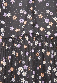 Robe noire à fleurs avec des fleurs blanches, violettes et pêches. Présente des boutons noirs et un bas froncé, sur fond à pois.