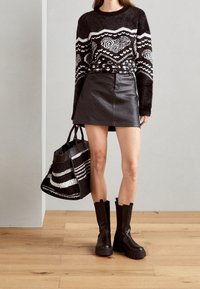 Schwarzer und weißer gemusterter Pullover, hochtaillierter Leder-Minirock, schwarze klobige Knöchelschäfte und eine gestreifte Tragetasche.