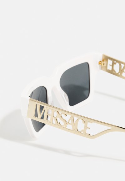 Occhiali da sole bianchi con lenti nere geometriche oversize, caratterizzati da un distintivo logo dorato "VERSACE" su ogni asta e una finitura lucida.