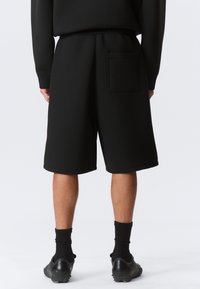 Schwarze Sweatshorts aus weichem Stoff, mit einer Gesäßtasche und einem elastischen Bund. Der Saum ist ohne zusätzliche Details verarbeitet.
