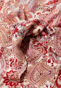 Bomuldsstoff med et blomster paisley mønster i rød, pink og blå på en beige baggrund, med en glat tekstur og levende farver.