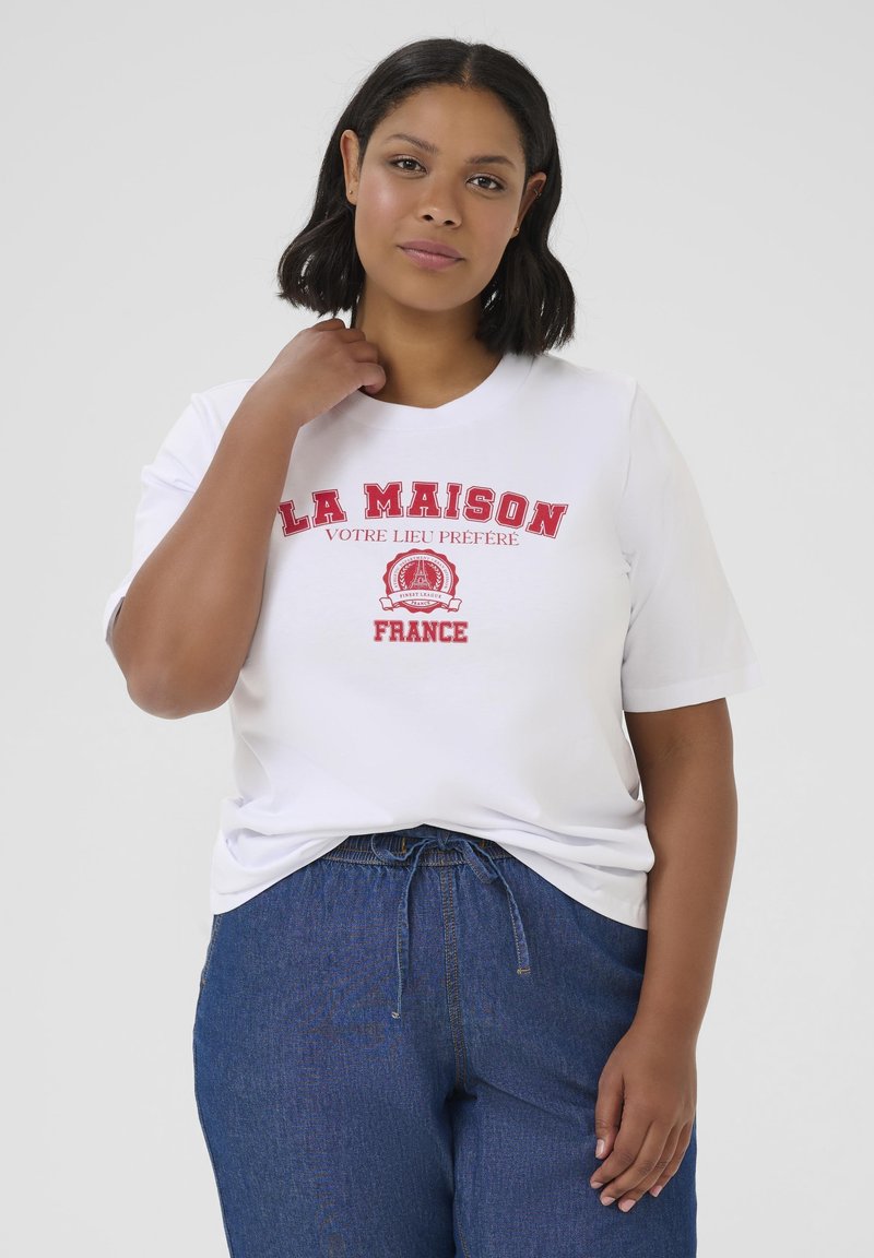 T-shirt blanc avec un texte brodé rouge "LA MAISON VOTRE LIEU PRÉFÉRÉ" et "FRANCE," col rond, manches courtes, associé à un pantalon en denim bleu.