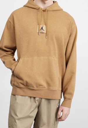 Beige hættetrøje med front kængurulomme og lille sort Jumpman logo patch, båret med lyse tan cargo bukser.