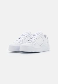 Vita lädersneakers med låg design, perforerad tåsidel, platta snören och en tjock, texturerad gummisula. Diskret branding på sidorna.