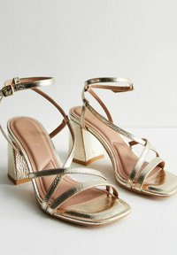 Gouden metallic sandalen met hakken, met een vierkante neus, een gestructureerde blokhak en een enkelgesp. Gladde voetbed in een lichte tan kleur.