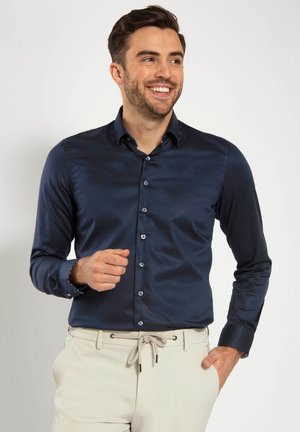 Navy blue, long-sleeve dress shirt with a smooth texture, button-down front, and contrasting light blue buttons. Worn with light-colored trousers.