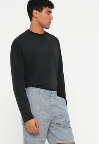 Black long-sleeve shirt with a round neckline, paired with blue and white striped shorts. Soft texture and relaxed fit.