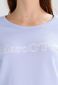 Felpa azzurra con collo a coste e testo ricamato in bianco "Marc O'Polo" esposto in modo prominente sul petto.