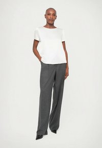 Blusa branca de mangas curtas combinada com calças cinzentas feitas à medida. A blusa tem decote redondo; as calças apresentam um corte de perna reta.