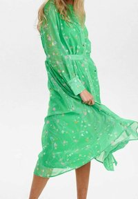 Grön, genomskinlig skjortklänning med blommönster, långa ärmar och ett knytbälte. Tyget har en flödande textur och en halvlång design.