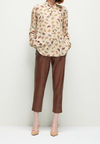 Camisa de seda beige impresa con un patrón de paisley, combinada con pantalones cortos de imitación de cuero marrón de cintura alta y zapatos de tacón beige.