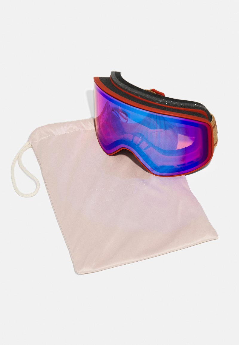 Skibrille mit einem großen lila getönten Glas, rotem Rahmen und schwarzem Schaumstoffpolster. Enthält einen weichen rosa Aufbewahrungsbeutel mit Logo.