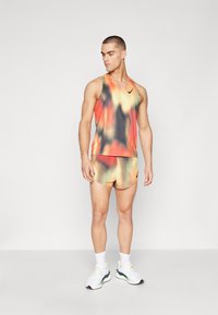 Débardeur sans manches et short Nike dans un mélange multicolore d'orange, de vert et de noir, offrant un tissu respirant et un logo central.
