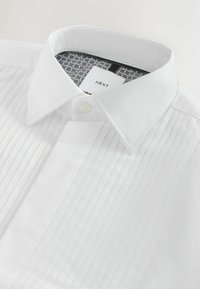 Camisa blanca de vestir con frente plisado, cuello clásico y cierre de botones. El interior del cuello tiene un forro con un patrón geométrico.