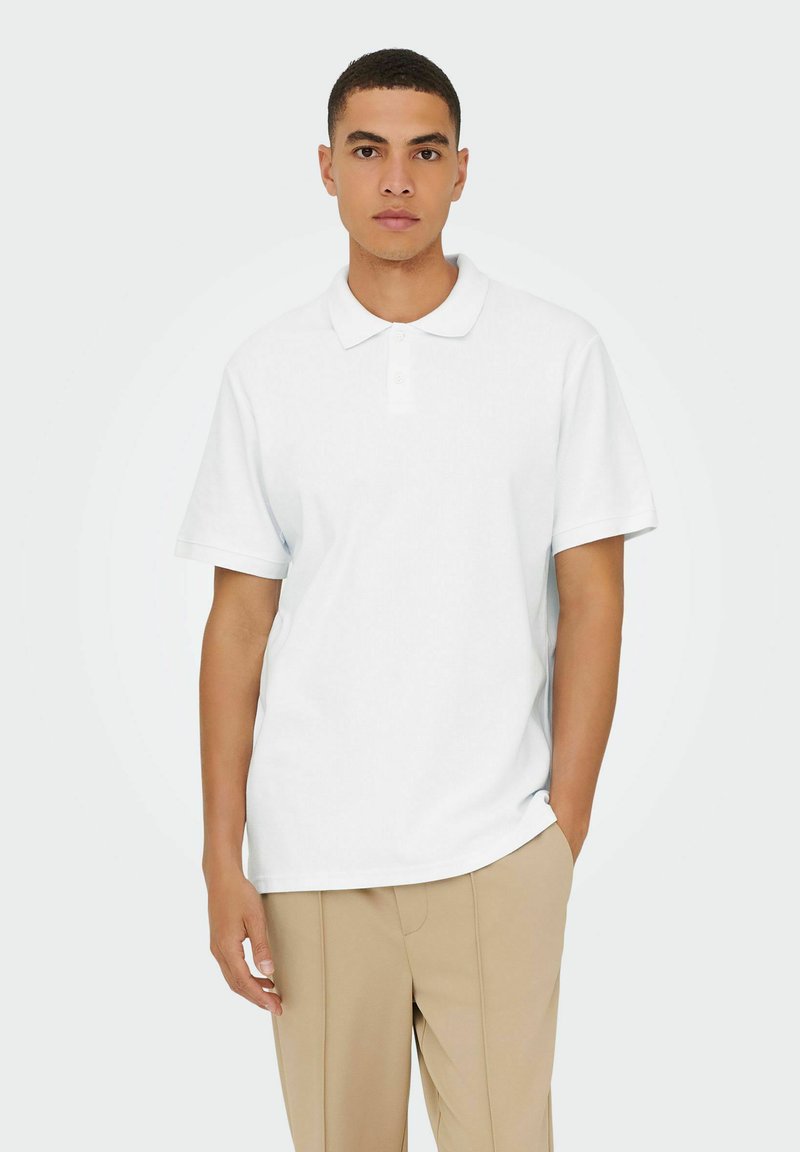 Hvid polo skjorte med korte ærmer, krave og tre knapper. Regular fit med glat tekstur, parret med beige bukser.