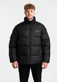Zwarte gewatteerde jas van nylon met doorgestikte secties, hoge kraag, voorrits en klein logo aan de linkerzijde.