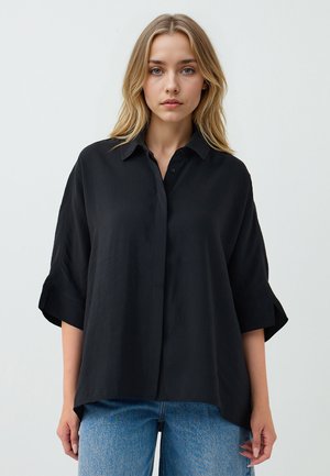 Black short-sleeve button-up shirt in a lightweight fabric with a relaxed fit and folded cuffs, paired with blue straight-leg jeans.