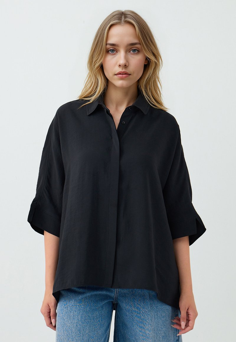 Black short-sleeve button-up shirt in a lightweight fabric with a relaxed fit and folded cuffs, paired with blue straight-leg jeans.