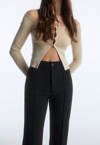 Haut beige côtelé à épaules dénudées avec détails de boutons et un devant court, associé à un pantalon noir taille haute avec une fermeture à un bouton.