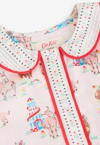 Blusa maniche corte in cotone rosa chiaro con un motivo animale giocoso, rifinitura del colletto rossa e chiusura a bottoni con ricamo decorativo nero.